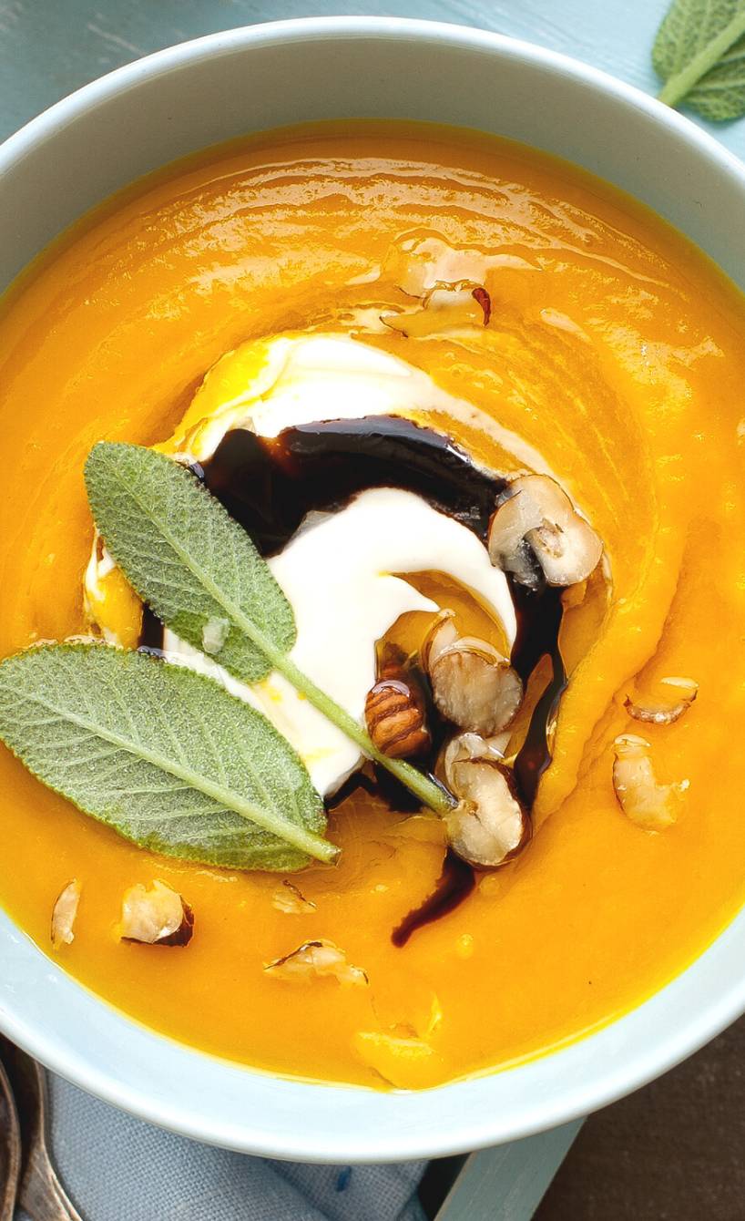 Kürbis-Apfelsuppe in zwei Suppenschalen auf einem Tisch, daneben baguette