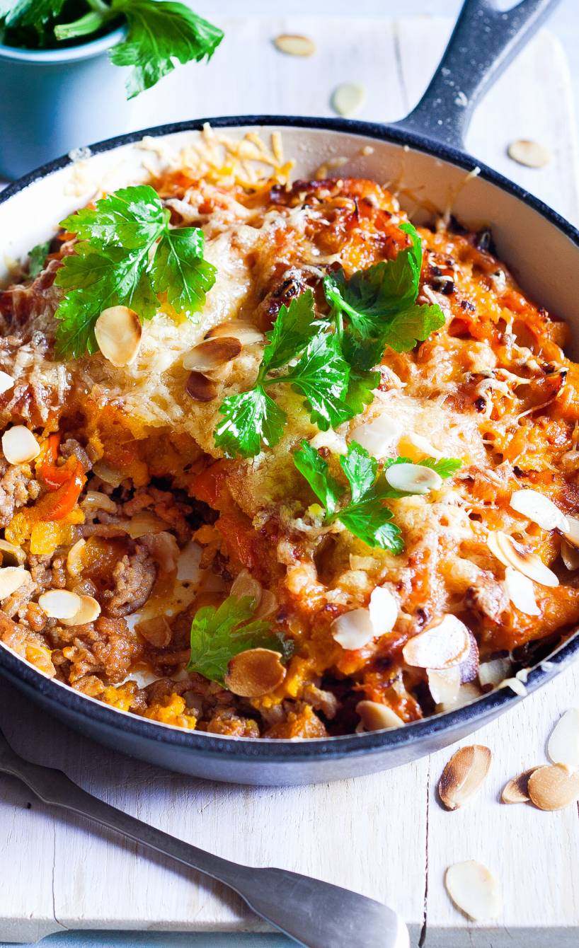 Kürbis-Hackauflauf in einer Pfanne auf einem Holztisch, daneben Basilikum