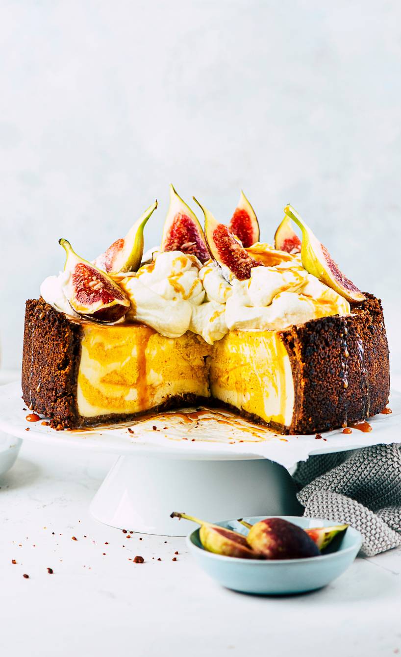 Kürbis-Käsekuchen auf einer Kuchenplatte getoppt mit Feigen, daneben Karamellsoße