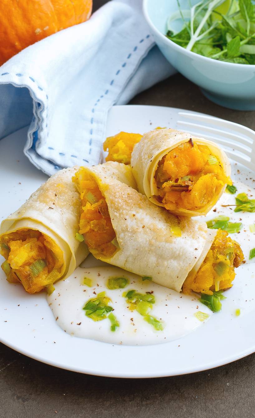 Cannelloni gefüllt mit Kürbis-Lauch-Mischung übereinander auf einem Teller, daneben ein Hokkaidokürbis