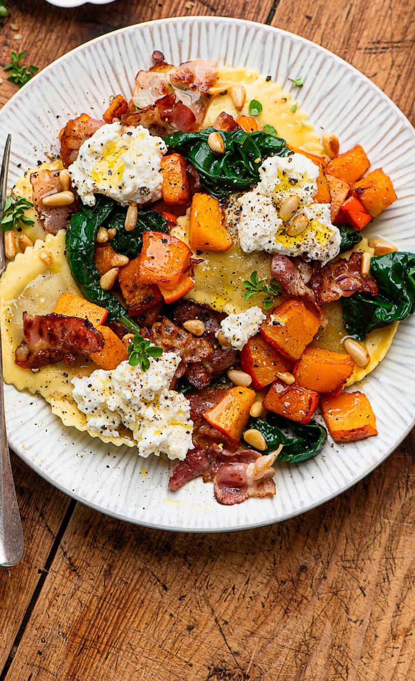 Kürbisravioli auf einem Teller getoppt mit Spinat, Pancetta und Ricottaflocken