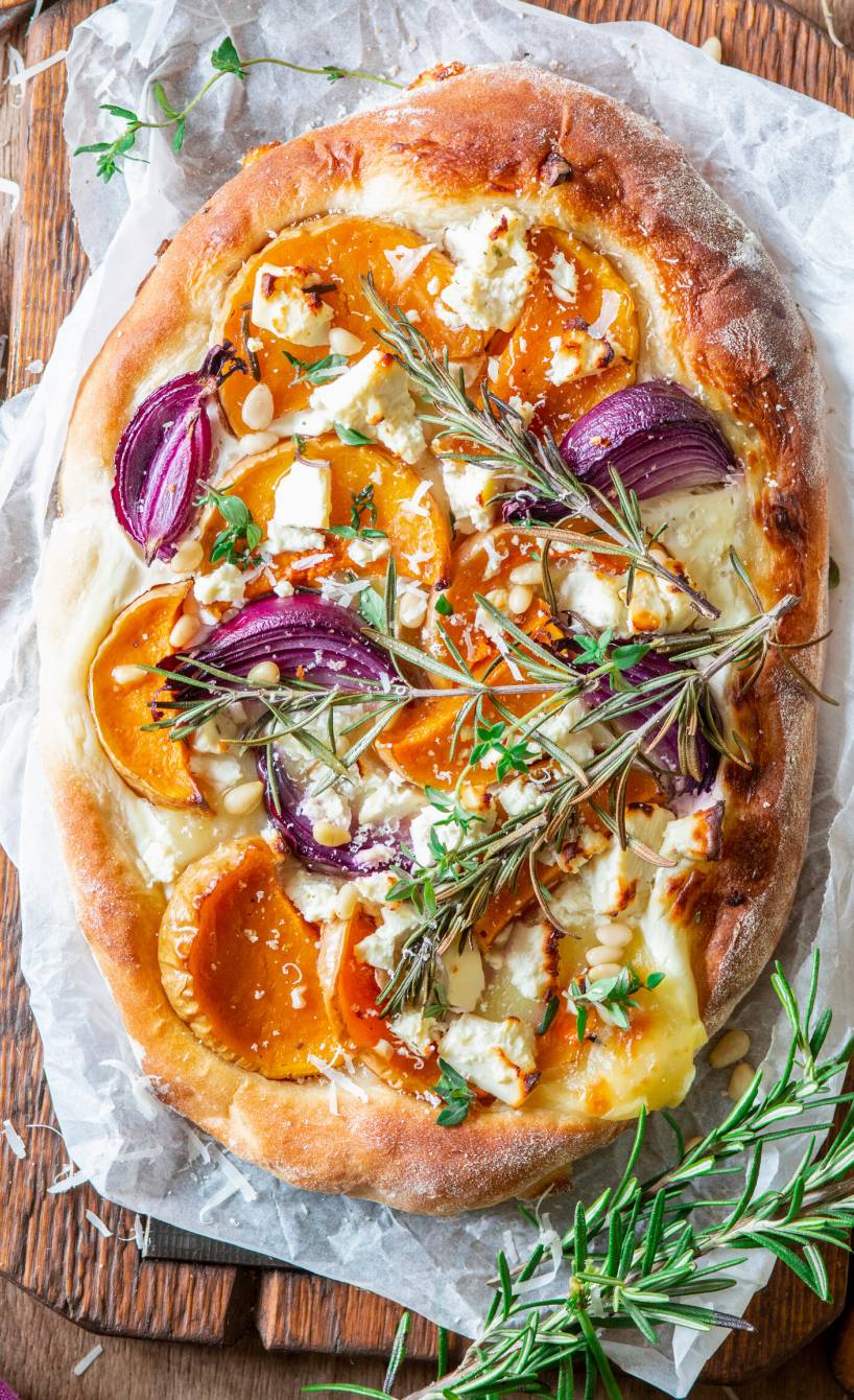 Kürbispizza mit Feta und Zwiebeln auf einem Holzbrett garniert mit einem Rosmarinzweig