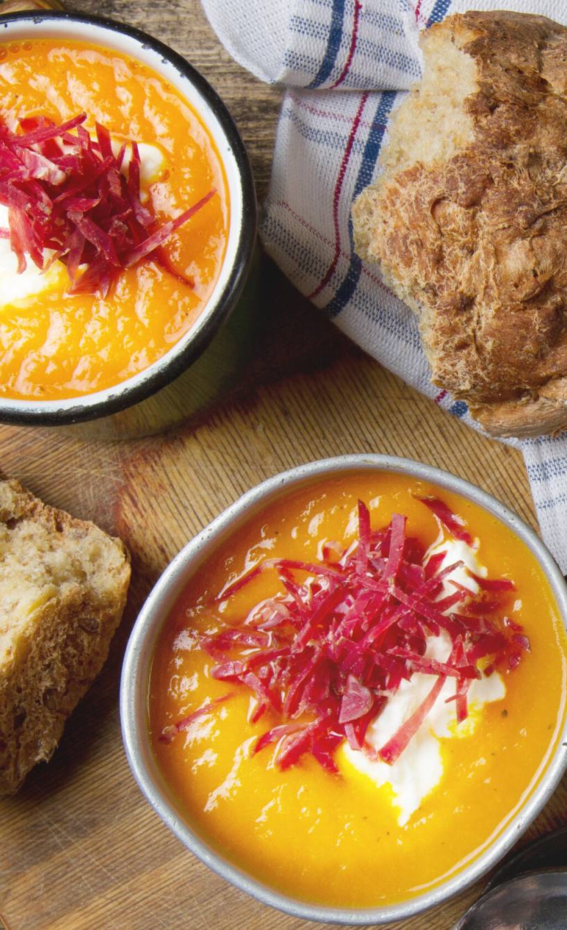 Kürbissuppe in zwei Suppenschüsseln auf einem Tisch, daneben Brot