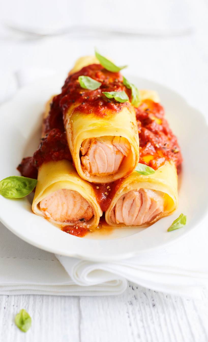 Drei Lachs-Canneloni gestapelt auf einem Teller, darauf Tomatensoße und Basilikum