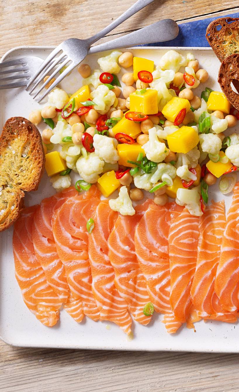Lachs-Carpaccio angerichtet mit Blumenkohl-Mango-Salat und Brotchips auf einem Vorspeisenteller