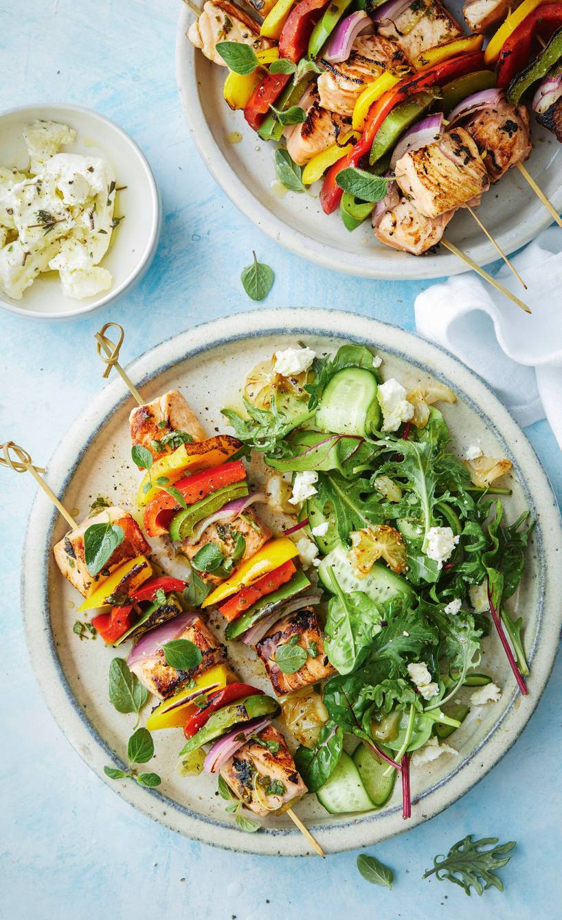 Gegrillte Lachs-Gemüse-Spieße auf einem Teller, daneben Salat und gegrillten Zitronen