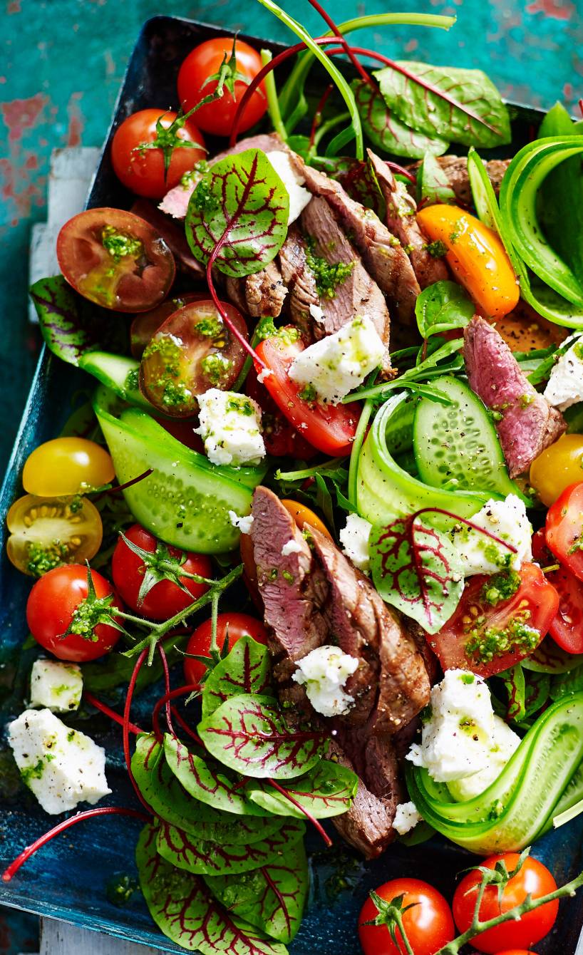 Mangold-Salat mit Tomaten, Lamm, Feta und Pesto auf einem rechteckigen Teller