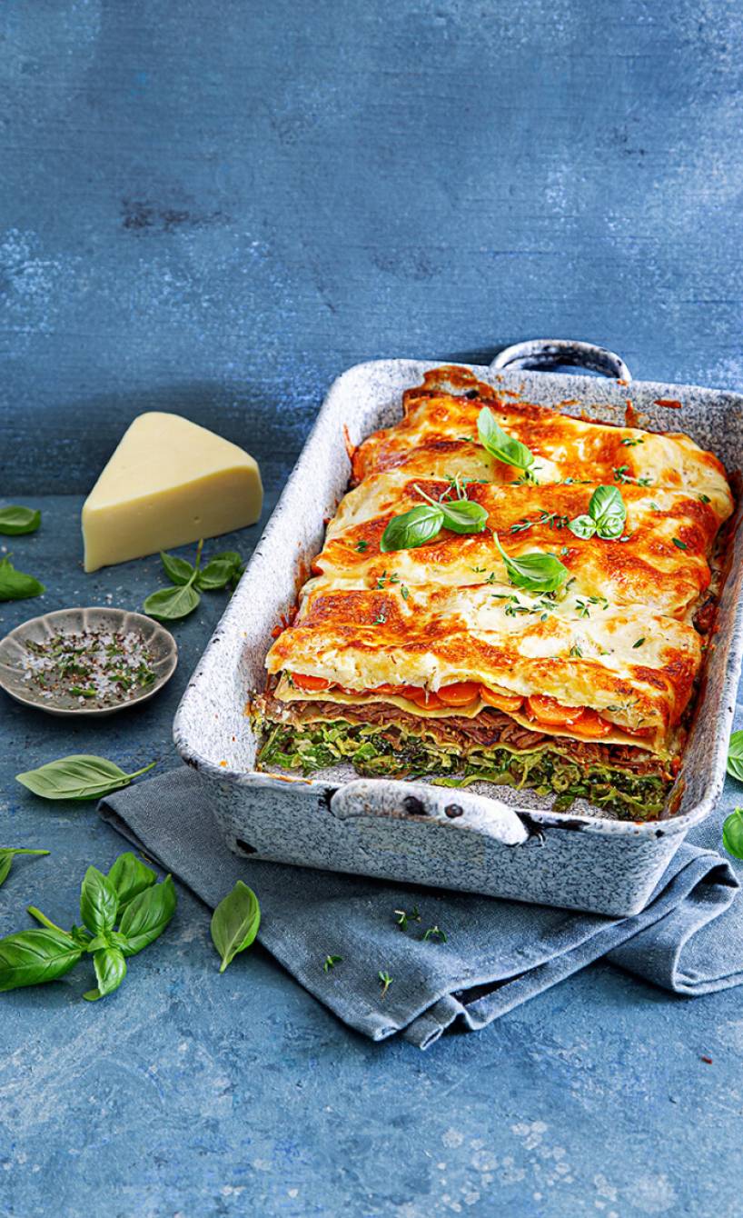 Wirsinglasagne mit Rinderbraten angeschnitten in einer Auflaufform, daneben Parmesan auf einem Tisch