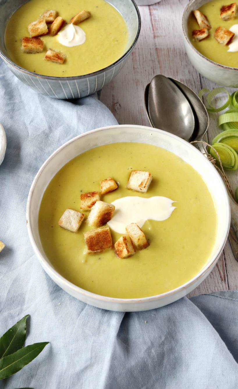 Lauchcremesuppe in mehreren Suppenschüsseln getoppt mit einem Klecks Crème fraîche und Croûtons auf einem Holztisch