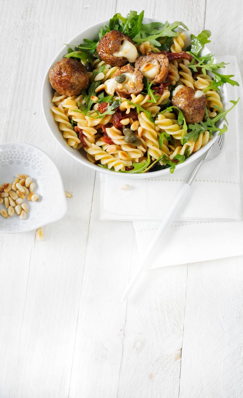 Fusilli-Salat in einer Schüssel mit Rucola, getrockneten Tomaten und Hackbällchen getoppt