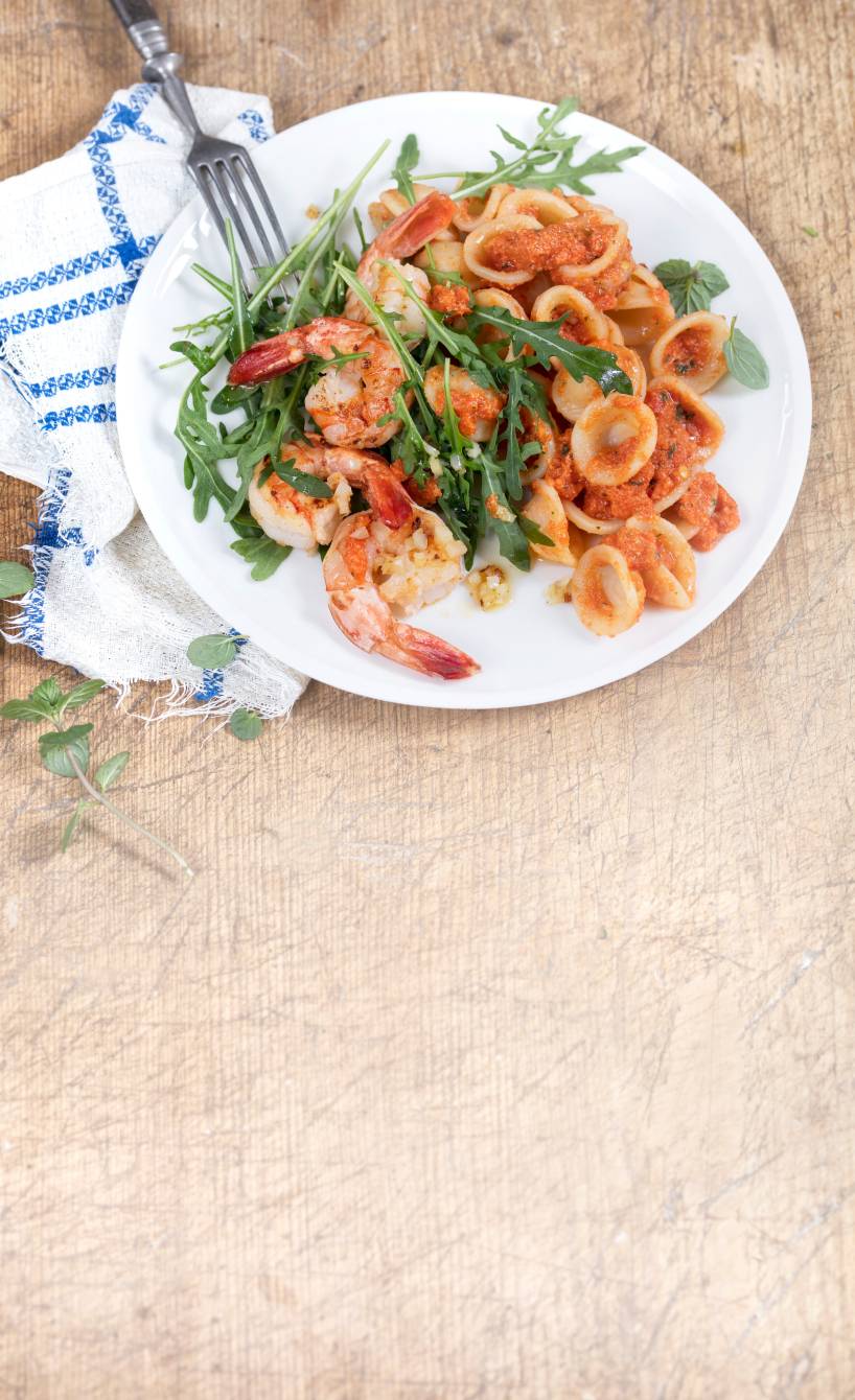 Nudelsalat mit Garnelen, Rucola und roter Sauce auf einem Teller