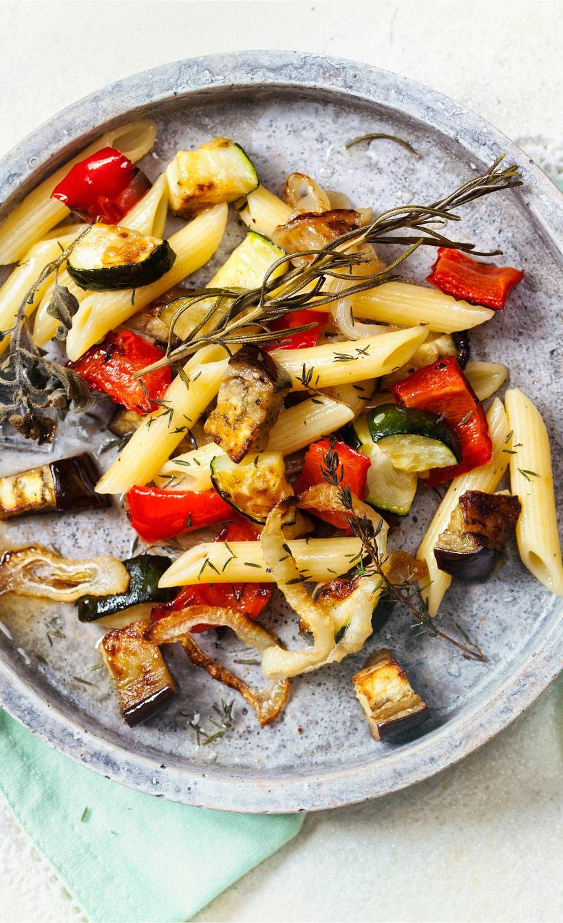 Nudelsalat mit Ofengemüse aus Zucchini, Aubergine und Paprika garniert mit Kräutern auf einem Teller