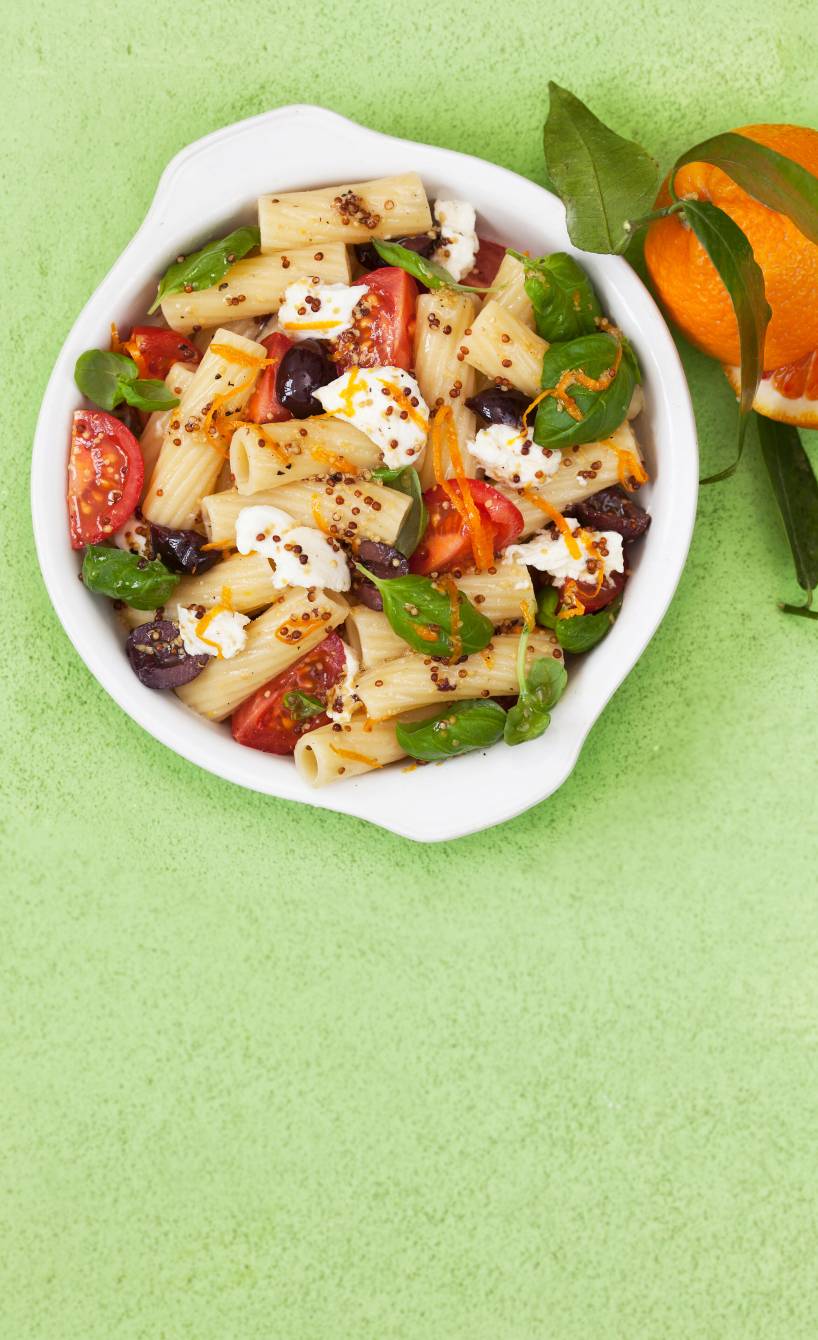 Nudelsalat in einer Schale mit Tomaten, Mozzarella und Basilikum, die Senfkörner des Dressings gut erkennbar