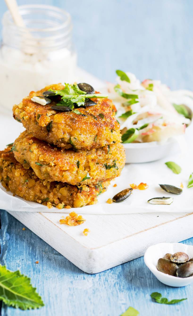 Drei gestapelte Linsen-Bratlinge angerichtet neben Apfel-Kohlrabi-Salat auf einem Teller