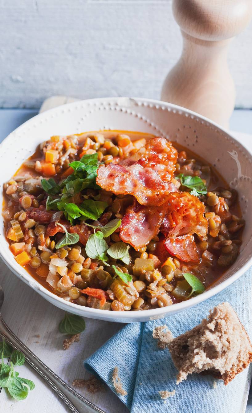 Italienischer Linseneintopf in einer Suppenschüssel getoppt mit Speck und frischen Kräutern