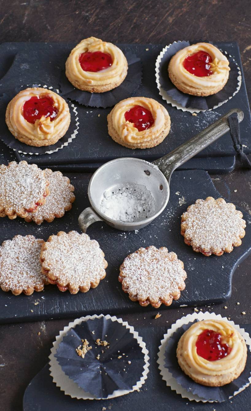 Linzer Plätzchen auf einer Schieferplatte, daneben Konfitüre und Puderzucker auf einem Tisch