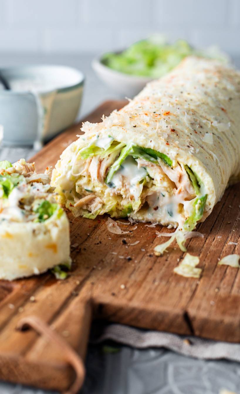 Low-Carb-Wrap aus Mozzarella, Ei und Quark angeschnitten mit Füllung aus Pute und Salat auf einem Holzbrett