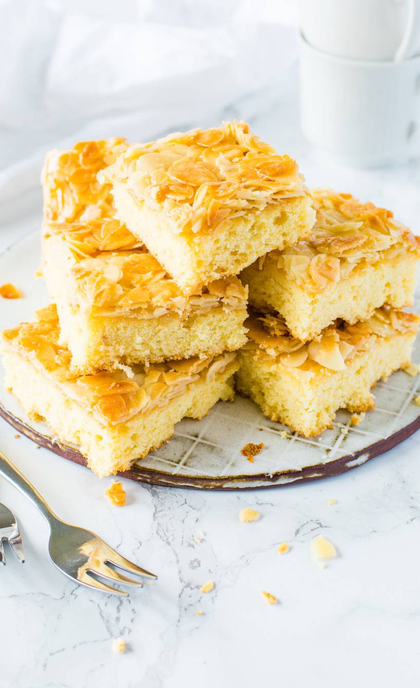 Mehrere Stücke Butterkuchen mit Mandeln vom Blech gestapelt auf einer Kuchenplatte