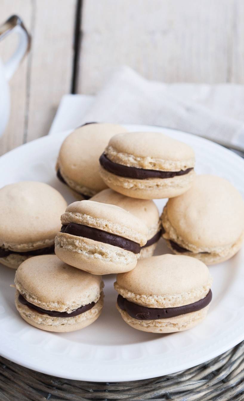 Mandelgebäck mit Schokofüllung auf einem Teller, daneben eine Kaffeetasse auf einem Tisch