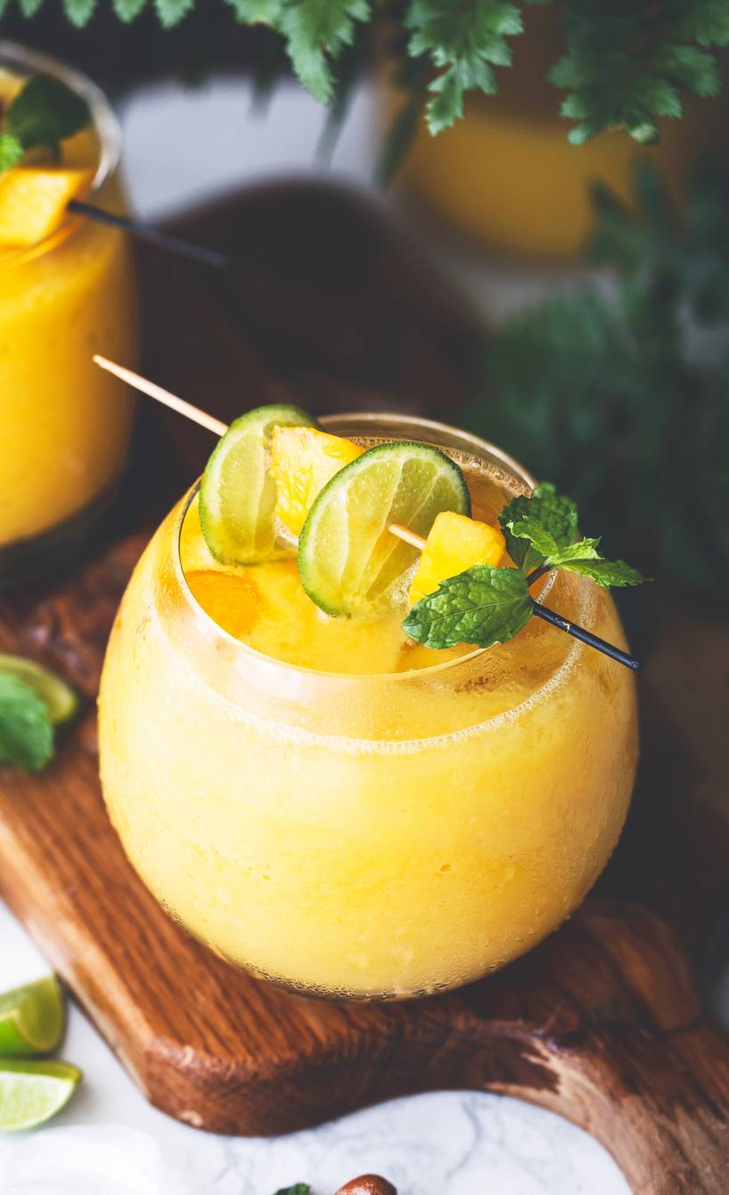 Gelber Smoothie mit Mango und Kurkuma in zwei Gläsern garniert mit Minze