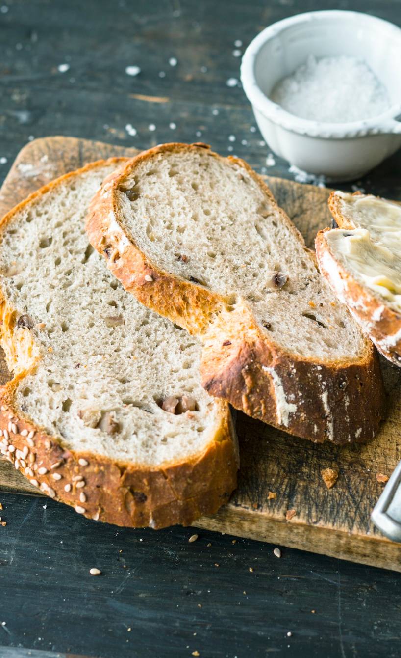 Scheiben von Sauerteigbrot auf einem Holzbrett, daneben Butter und Salz