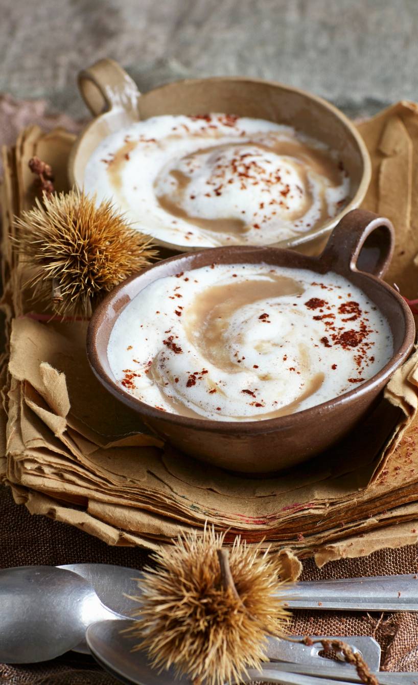  Maronensuppe mit Milchschaum-Haube und Schokoladentopping in zwei Suppenschalen auf einem festlich dekorierten Tisch