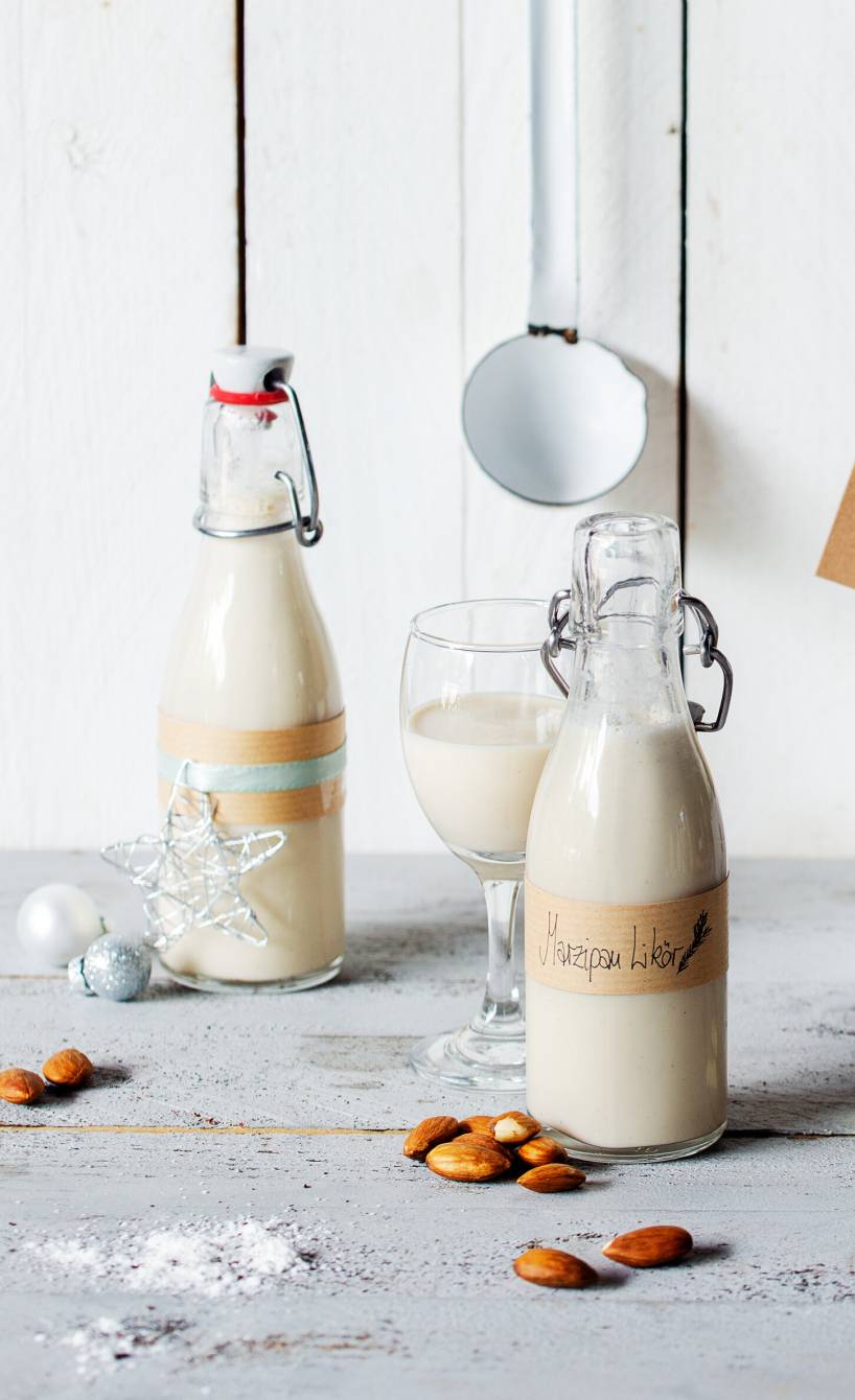 Marzipanlikör in Flaschen abgefüllt und mit Geschenkanhängern auf einem Holztisch