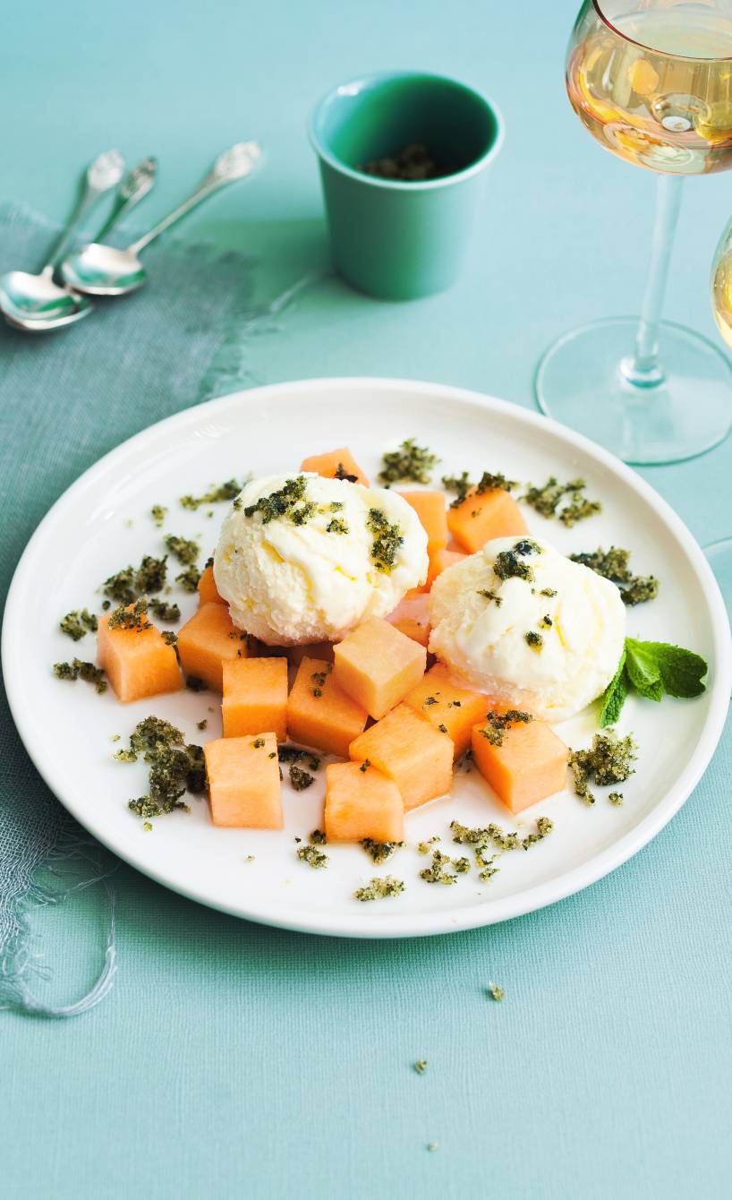 Zwei Kugeln selbstgemachtes Limoncello-Eis angerichtet mit Melone und Minze auf einem Dessertteller