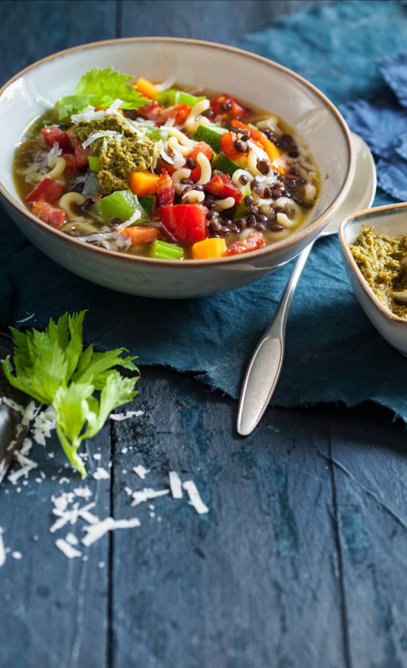 Minestrone mit Linsen, Nudeln und Gemüse in einer Suppenschüssel getoppt mit grünem Pesto
