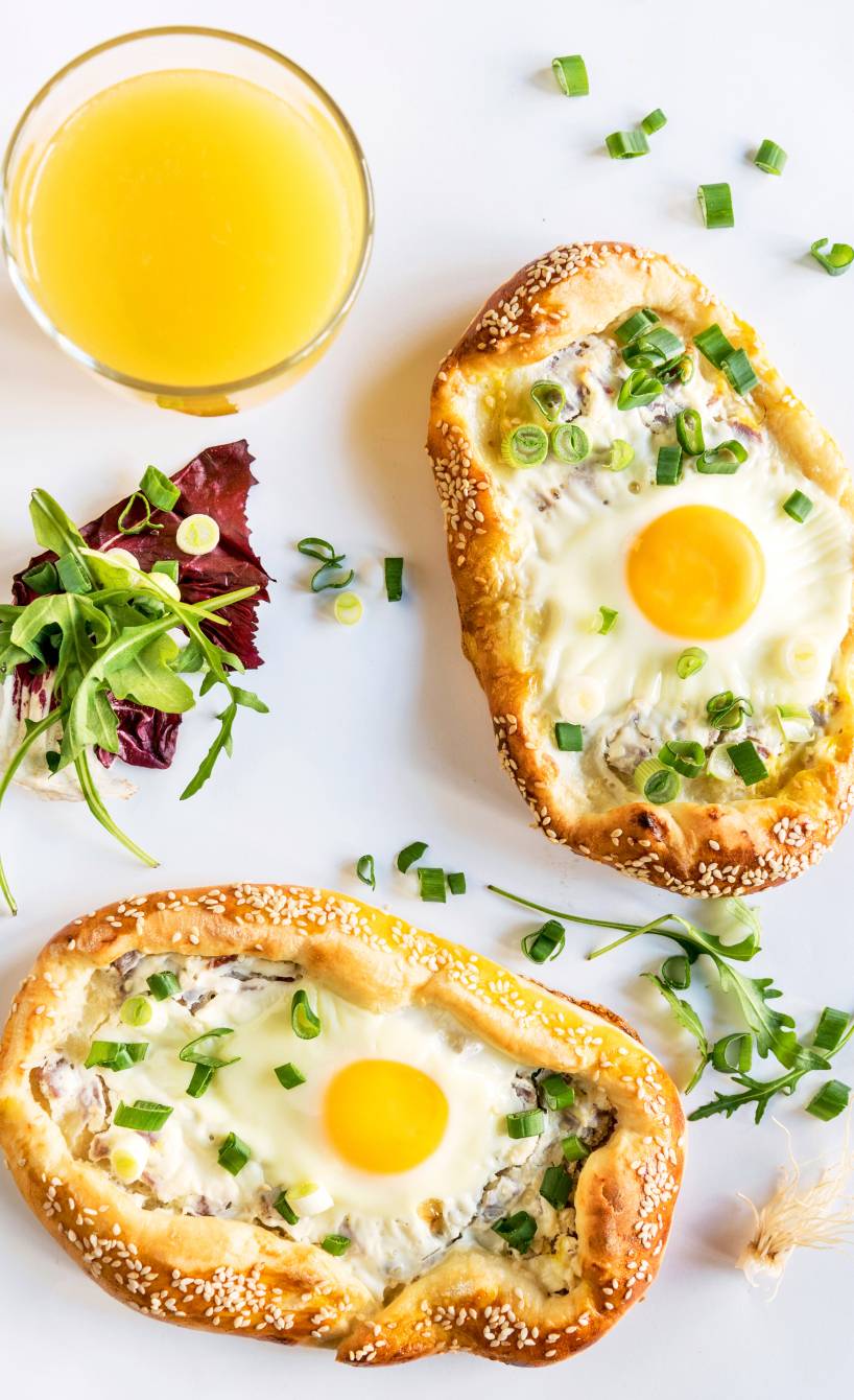 Zwei Minipizzen mit Eiern auf einem Tisch getoppt von frischen Kräutern