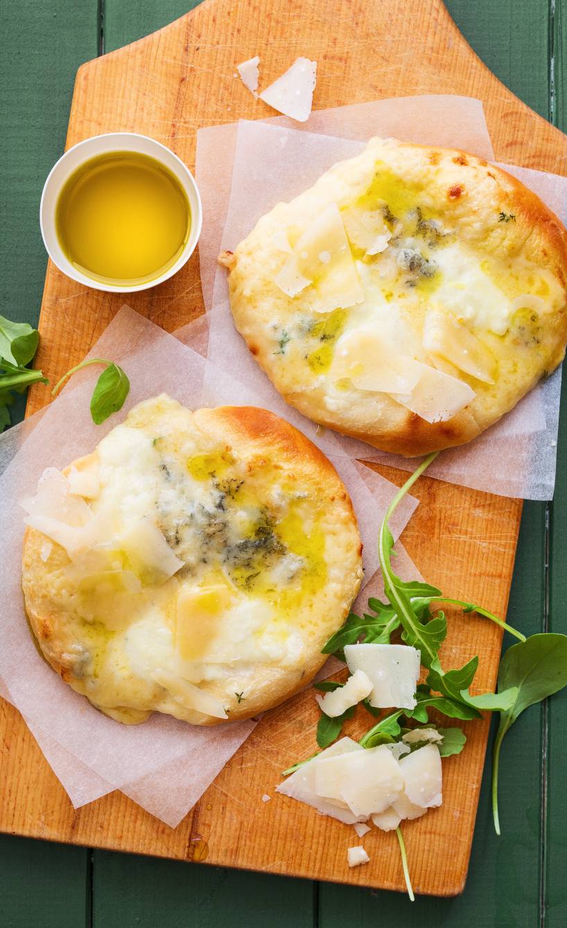 Zwei selbstgebackene Mini-4-Käse-Pizzen auf einem Holzbrett