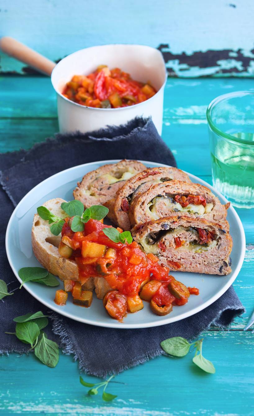 Vier Stücke Hackbraten mit Mozzarella-Gemüse-Füllung angerichtet auf einem Teller mit Ciabatta und Zucchini-Tomatensoße
