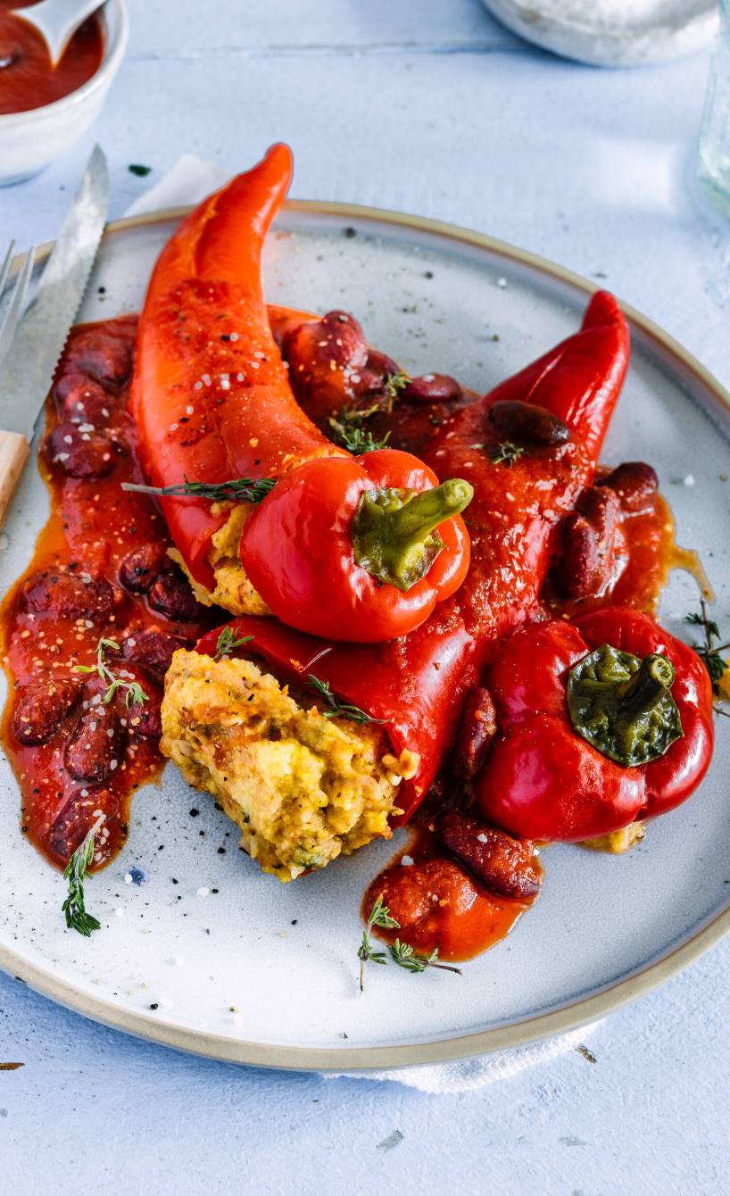 Drei vegan gefüllte Spitzpaprikas mit Polentafüllung auf einem Teller getoppt mit Bohnensauce