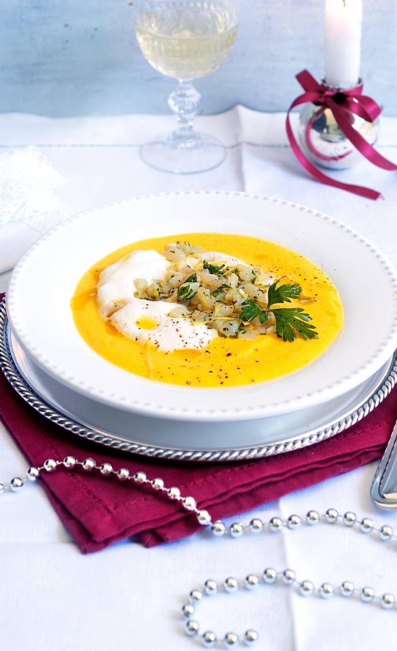 Goldene Apfel-Sellerie-Suppe in einem Suppenteller getoppt von Milchschaum und Jakobsmuschel-Tartar auf einem weihnachtlich dekorierten Tisch