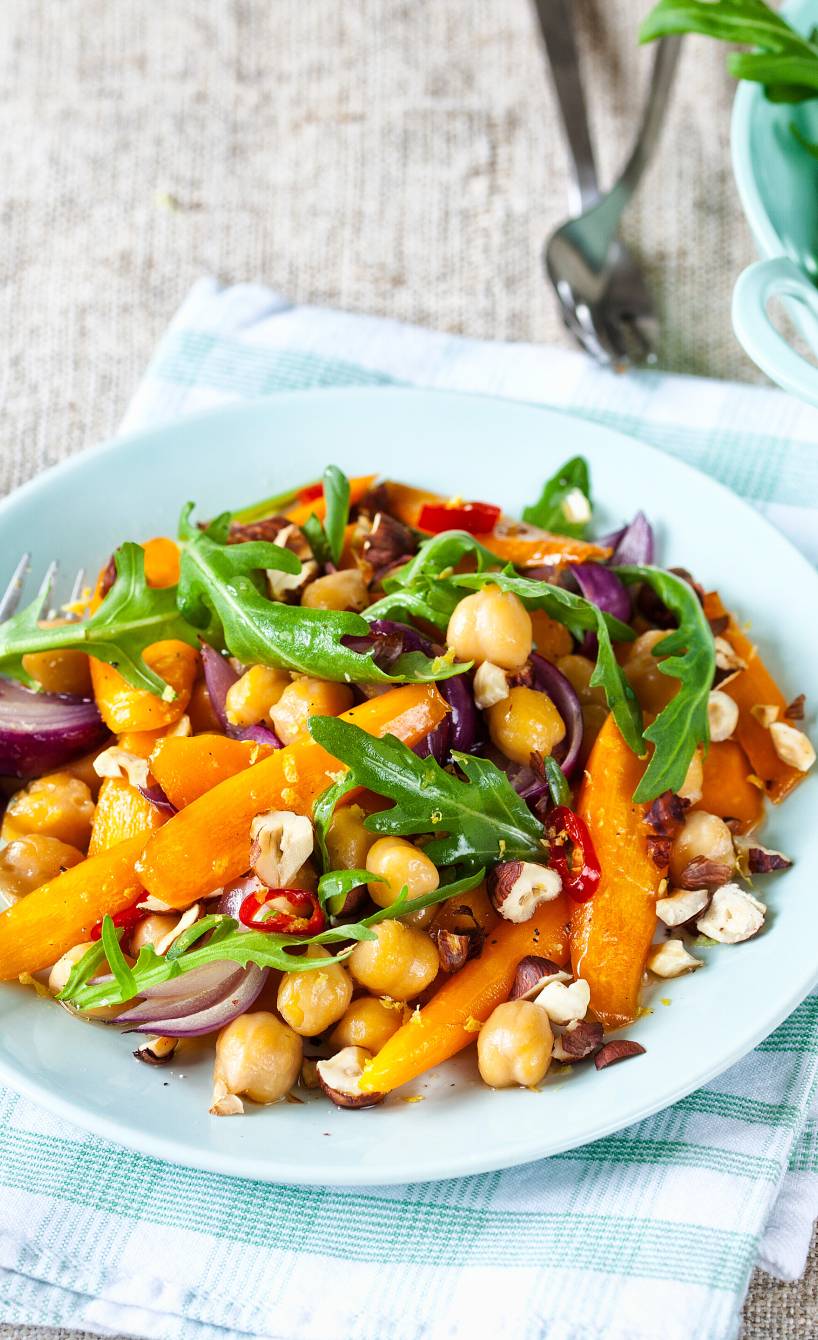 Karottensalat mir Kichererbsen und Rucola getoppt von Haselnüssen angerichtet auf einem Salatteller, daneben Vinaigrette