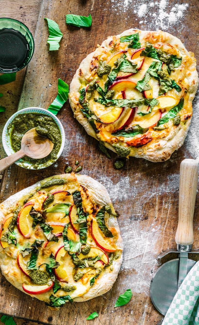 Pizza mit Nektarinen, Käse, Mangold und Pesto belegt auf einem Holzbrett