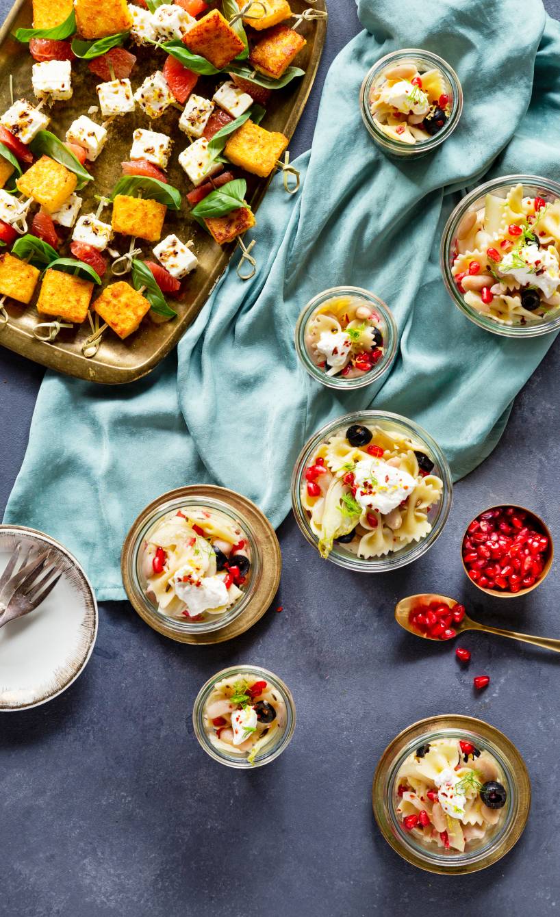 Nudelsalat aus Fusilli in Gläsern getoppt mit Ricotta und Granatapfelkernen auf einem Tisch