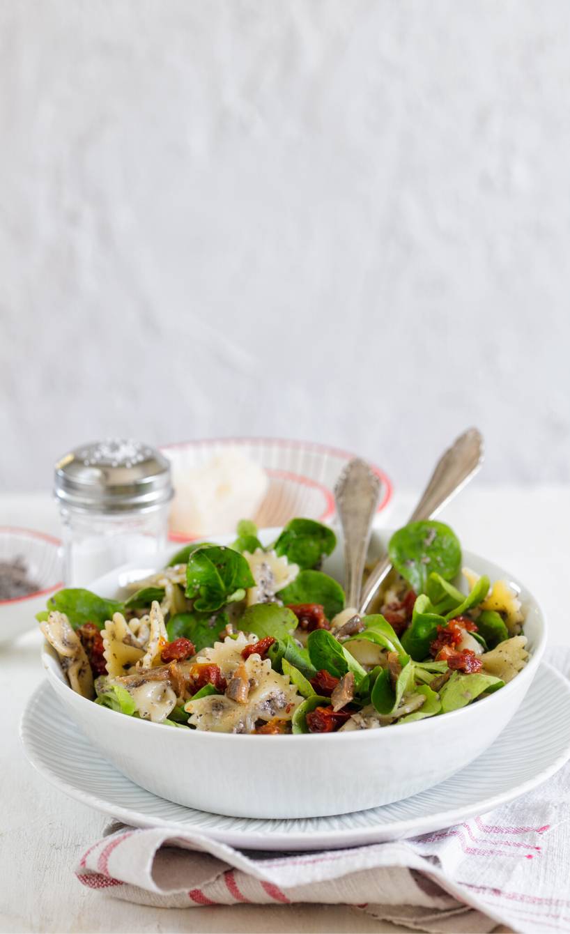 Nudelsalat aus Fusilli in einer Schüssel garniert mit Sardellen und getrockneten Tomaten