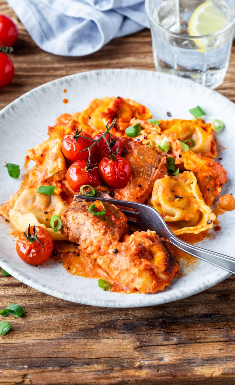 Ofenlachs und Tortellini in Tomaten-Sahne-Soße angerichtet auf einem Teller