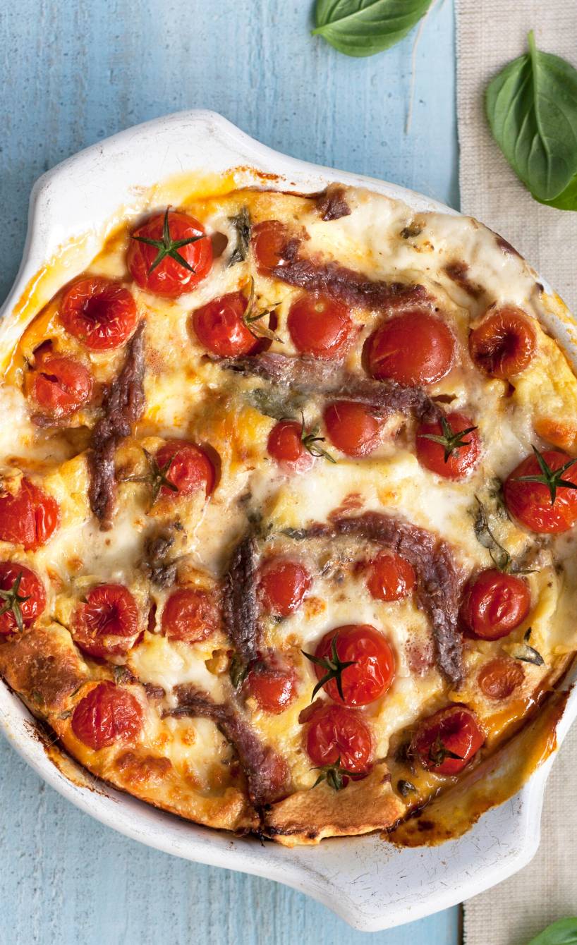 Ofenpfannkuchen in einer Auflaufform erkennbar sind Sardellen, Tomaten und Mozzarella
