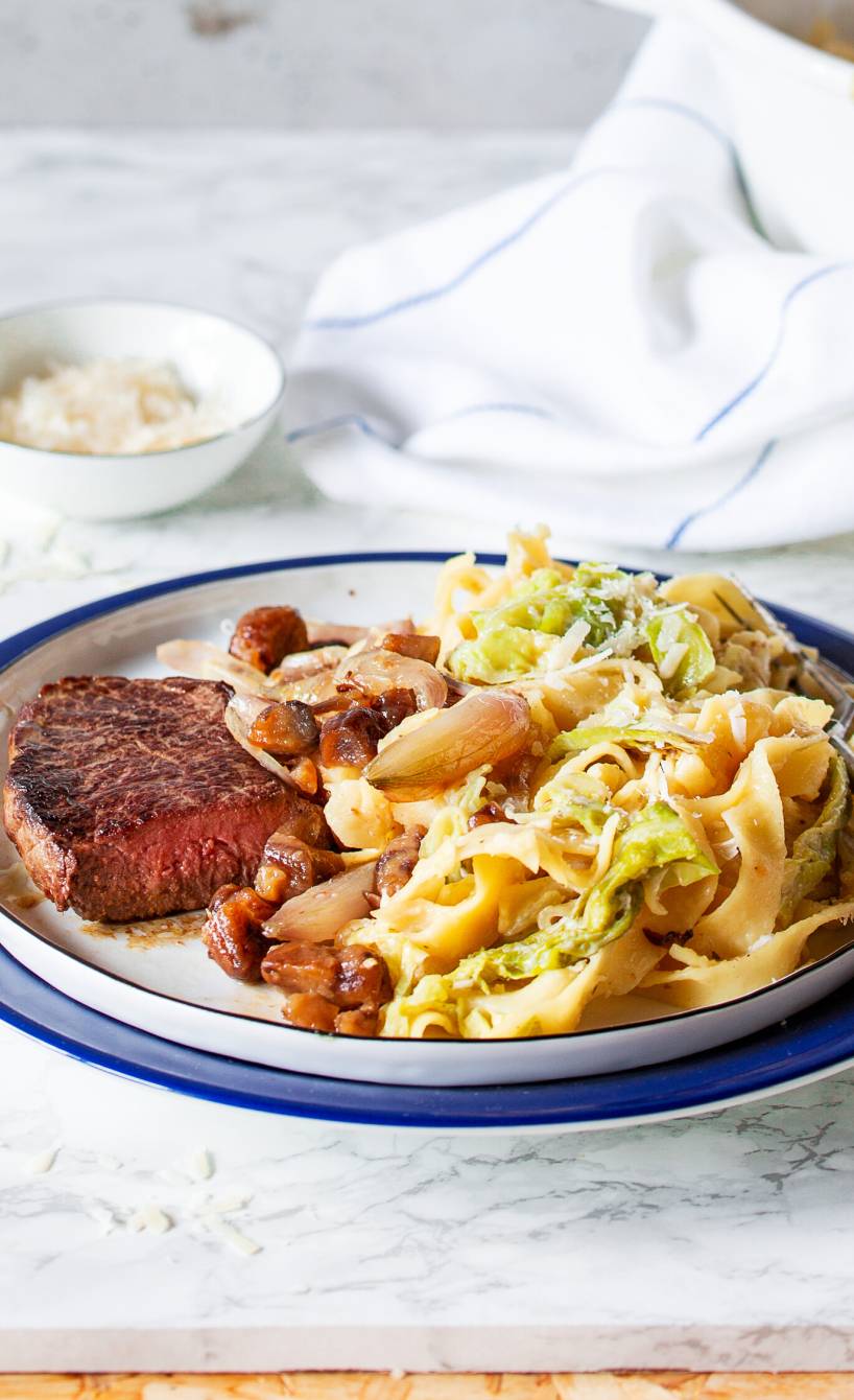 One-Pot-Bandnudeln auf einem Teller mit Wirsing und Soße, daneben Hüftsteak
