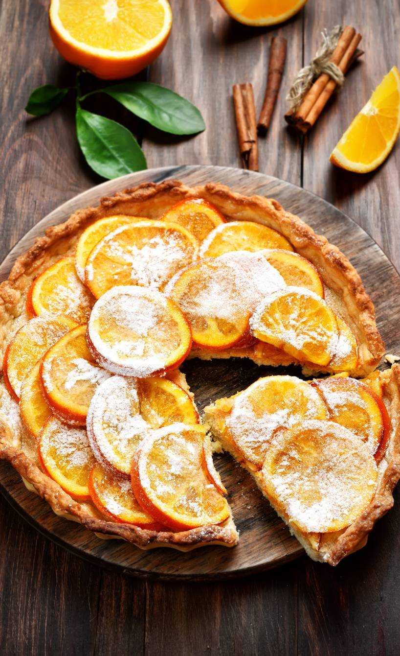 Angeschnittene Crostata mit Haselnussboden und Vanillecreme-Füllung getoppt von kandierten Orangenscheiben auf einem Kuchenteller
