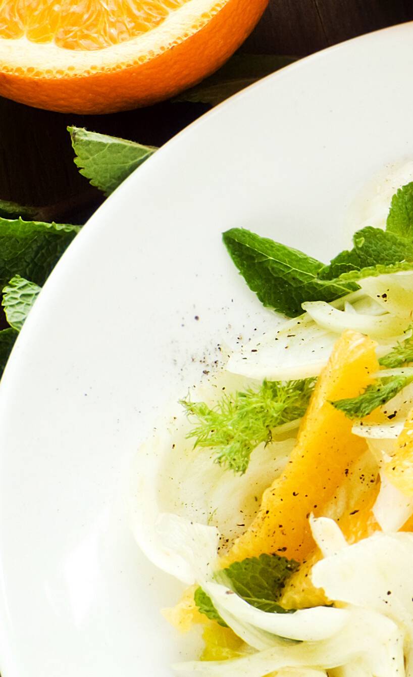Fenchelsalat mit Orangen auf einem Teller, daneben Minze