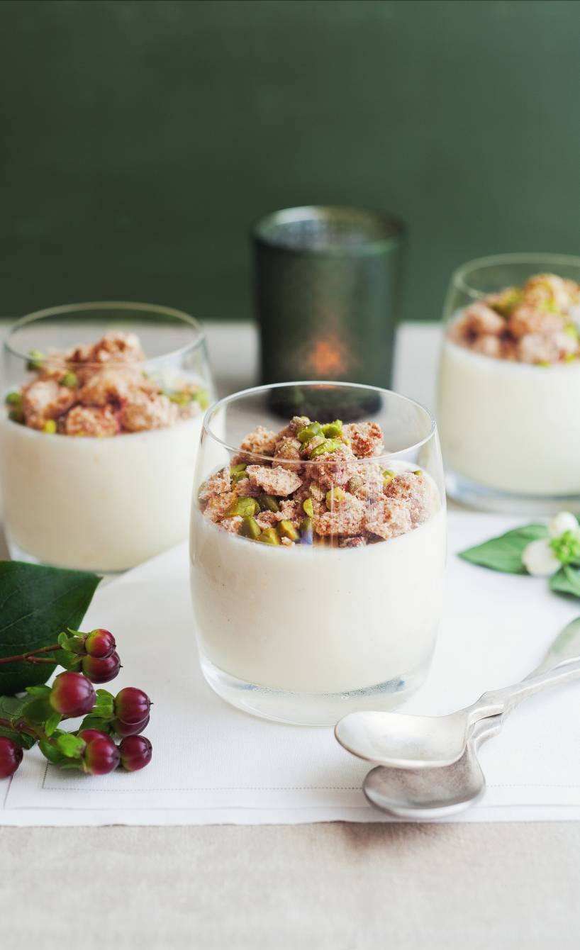 Joghurt-Mousse in drei Dessertgläsern getoppt mit Amarettini-Pistazien-Streuseln auf einem weihnachtlich dekorierten Tisch
