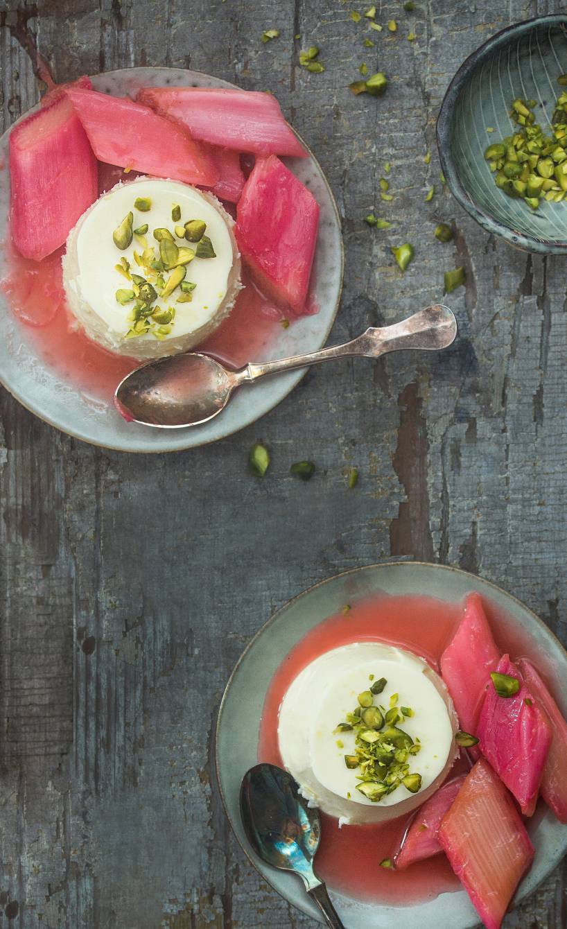 Zwei Portionen Panna Cotta mit Rhabarberkompott auf Desserttellern getoppt mit Pistazienkernen
