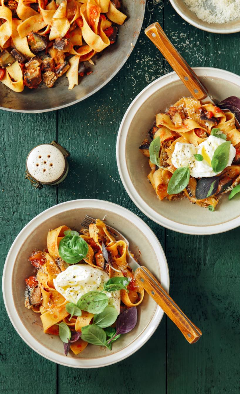 Pappardelle angerichtet mit Auberginensugo und getoppt von einer Burrata-Kugel auf einem Pastateller
