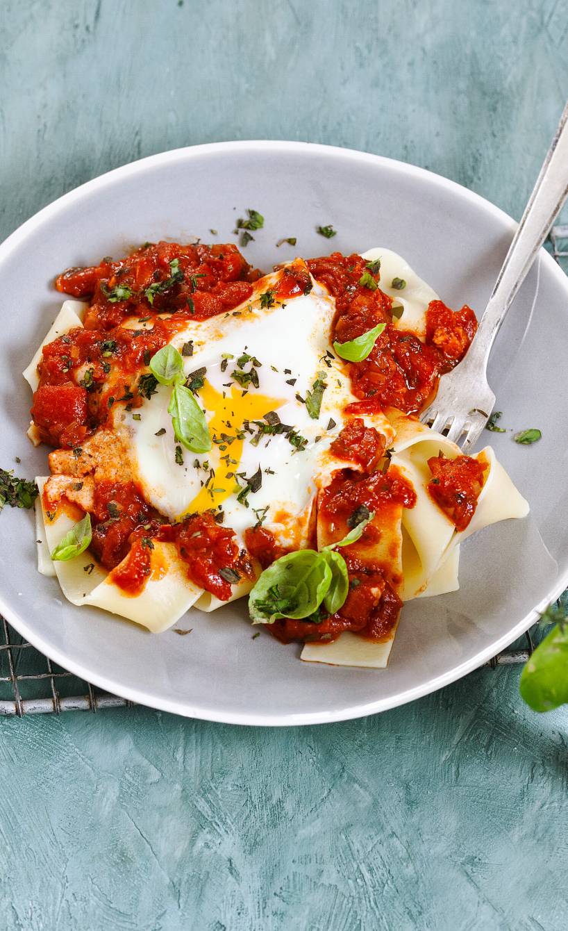 Bandnudeln auf einem Pastateller getoppt von Tomatensoße und Eiern