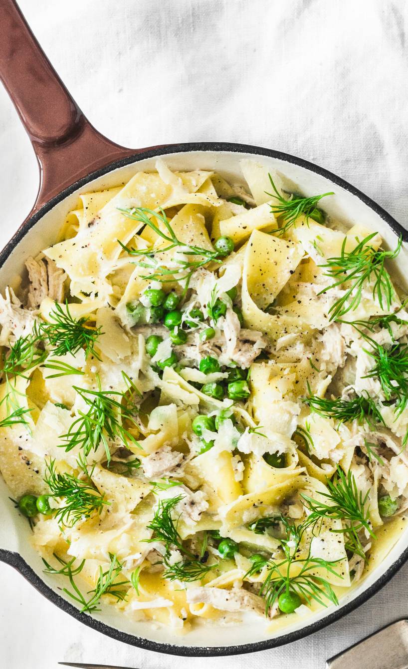 Pappardelle in einem Steiltopf getoppt mit Hähnchenragout, Erbsen und Fenchelgrün auf einem Tisch
