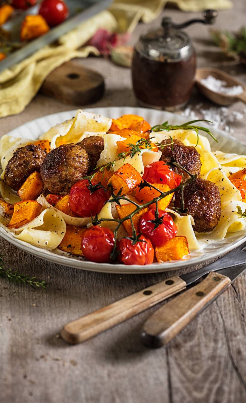 Pappardelle Bandnudeln auf einem Teller getoppt von Hackbällchen und gebackenen Kürbisstücken