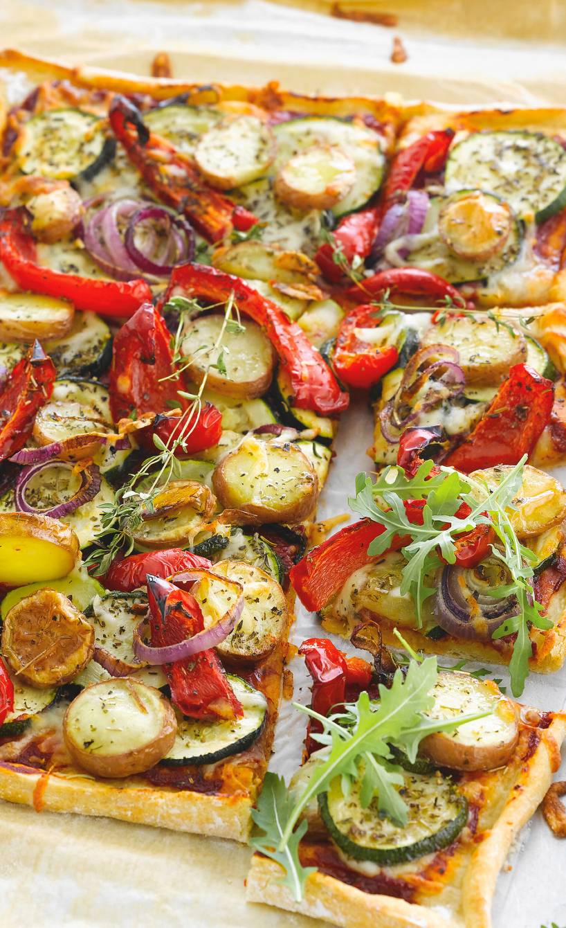 Vegane Pizza mit Zucchini, Paprika und Kartoffeln angeschnitten auf einem Backblech